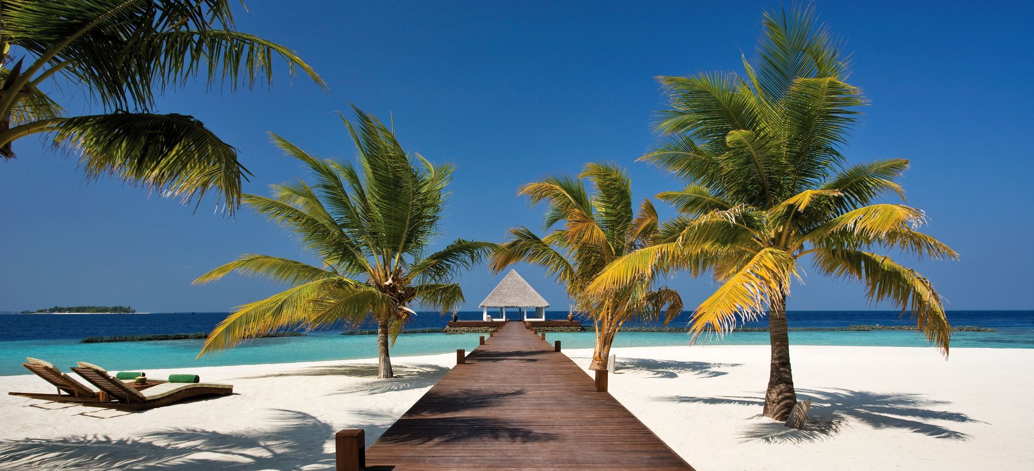 Ein palmenumsäumter Steg auf Strand und über der Lagune der Malediveninsel Coco Palm Bodu Hithi