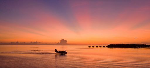 Ein Wasserflugzeug landet im Abendrot vor der Resortinsel Conrad Maldives