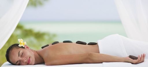 Frau genießt eine Hot Stone Massage mit Blume im Haar, direkt am Strand