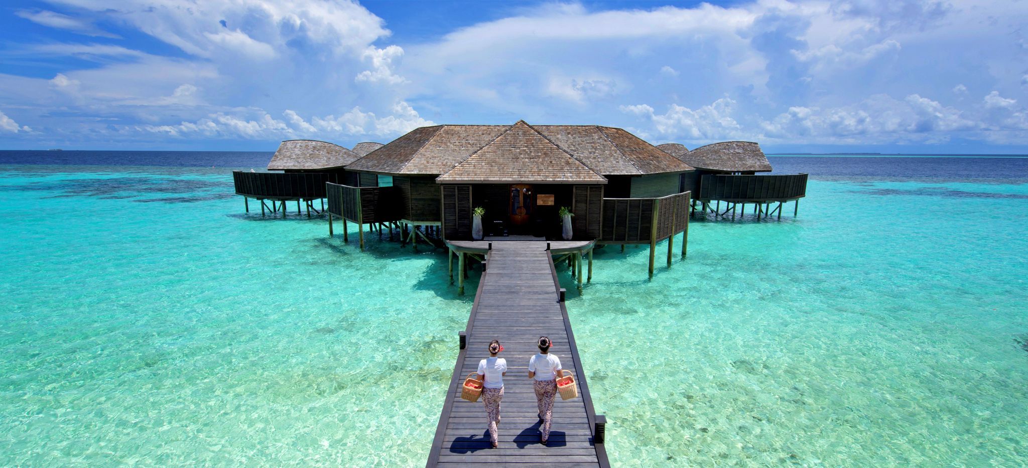 Zwei Masseurinnen laufen über einen Steg zum auf Stelzen in die Lagune gebautem Spa des Hotels "Lily Beach"