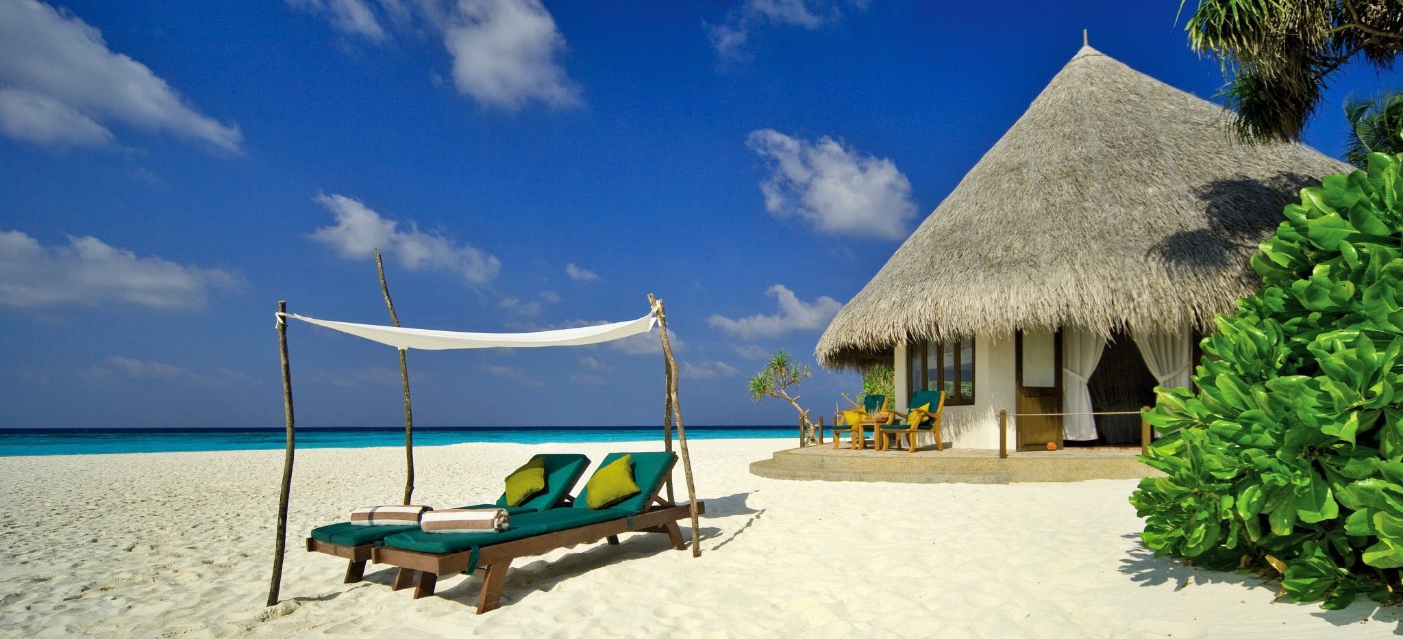 Eine Strandvilla mit einer Strandliege auf der Malediveninsel Coco Palm Dhuni Kolhu