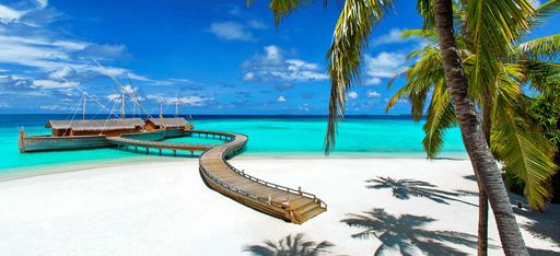 Ein weißer Sandstrand mit einem Steg, an dem ein Restaurant liegt, das aussieht wie die traditionellen Dhonis der Malediver