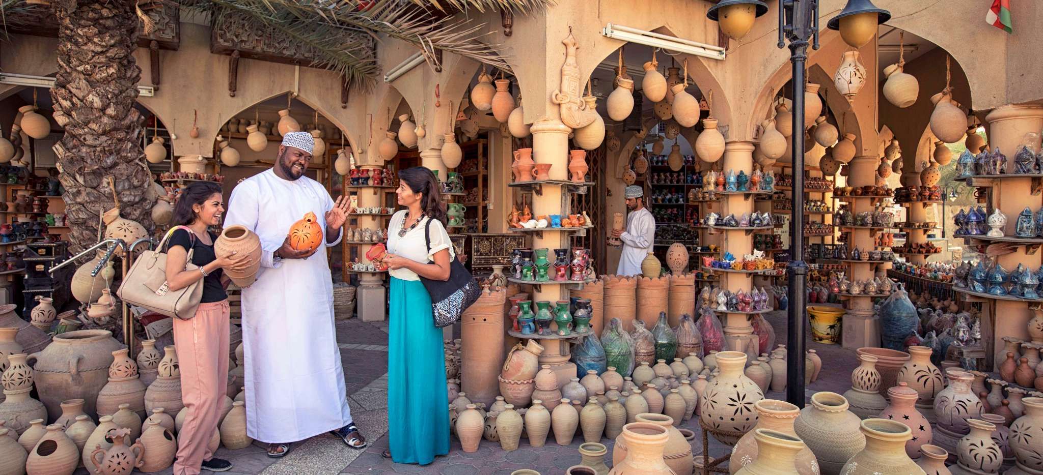 Zwei Touristinnen verhandeln mit einem Mann in traditioneller Kleidung auf dem Basar von Nizwa, Oman
