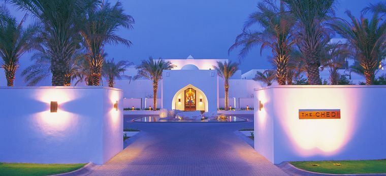 Eingang in das Hotel "The Chedi Muscat" mit Dattelbäumen und weißen Mauern, Nachtaufnahme