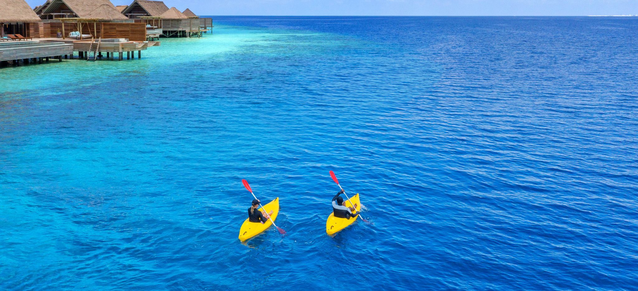 Paar in einzelnen Kajaks rudert vorbei an den Wasservillen des Waldorf Astoria Maldives, mit Blick auf das offene Meer