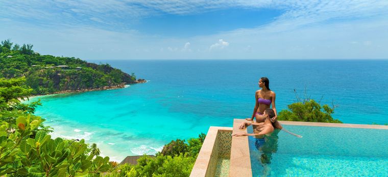 Paar badet in einem Infinity Pool mit Blick auf den Strand Petite Anse im Hotel Four Seasons Resort Seychelles