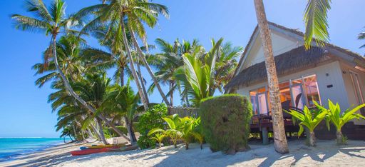Außensicht des Beachfront Bungalows des Little Polynesian Resorts mit Palmen und Kanus.