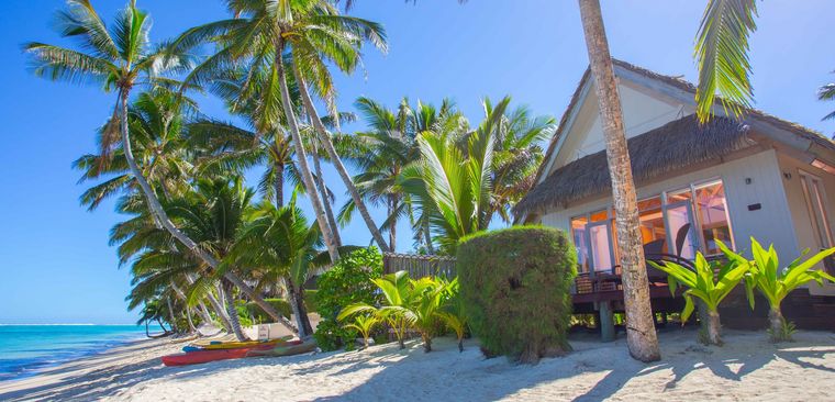 Außensicht des Beachfront Bungalows des Little Polynesian Resorts mit Palmen und Kanus.