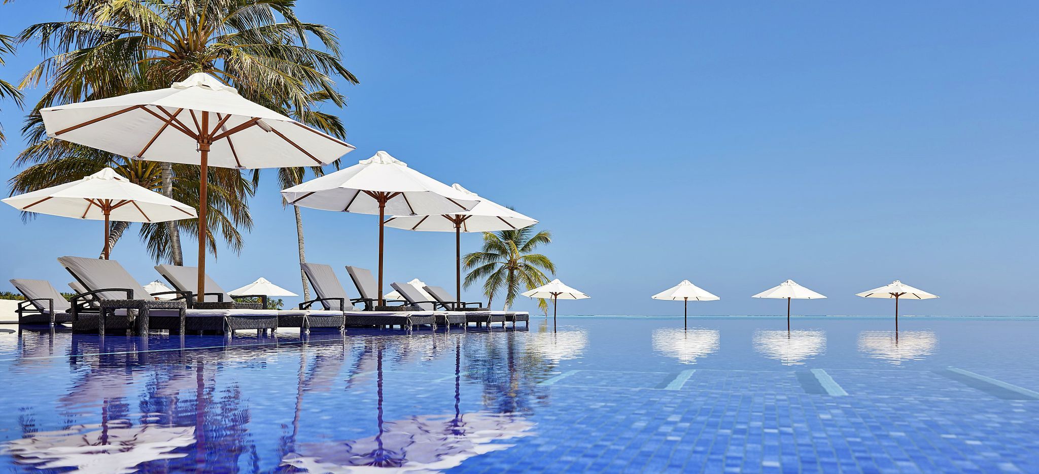 Ein Langer Pool mit Strandliegen und Sonnenschirmen im Hotel Conrad Maldives