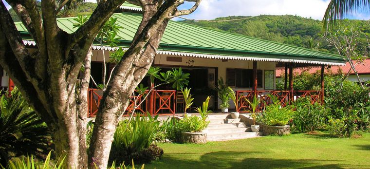 Ein großes Kolonialhaus mit grünem Dach durch einen tropischen Garten gesehen. Aufgenommen in der Villa Bambou auf den Seychellen