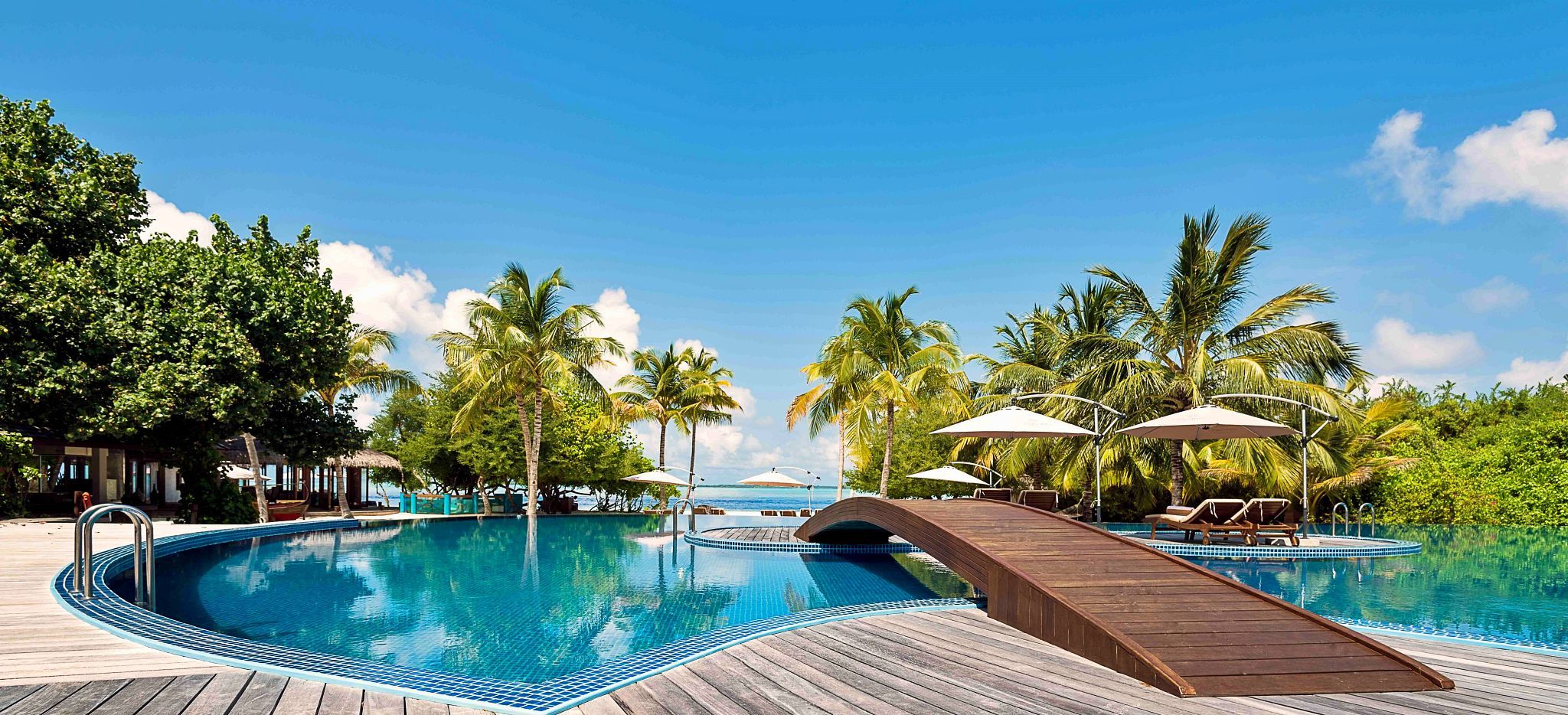 Ein Pool mit einer Holzbrücke, von Palmen umsäumt