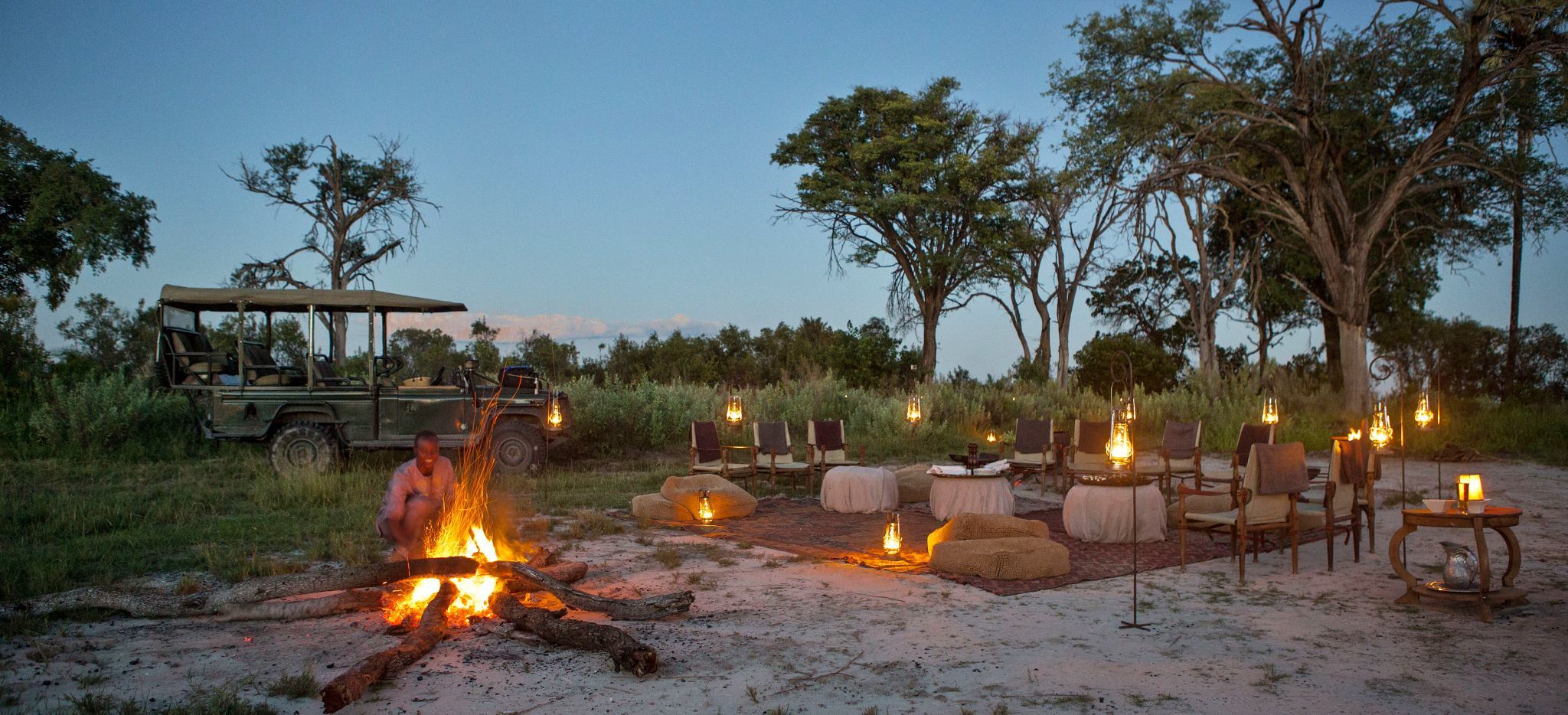 A guide is fanning a fire in the Okavango Delta, another is preparing a Dinner in the Wilderness.