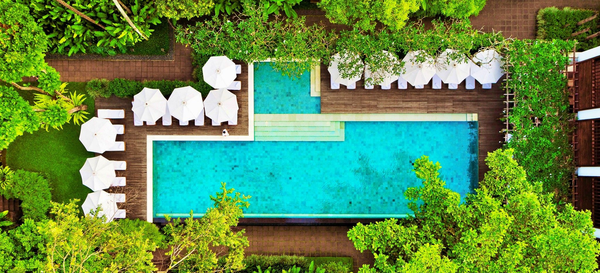 Ein Pool in einer Holzterrasse eingelassen, außern herum Sonnenschirme und Strandiegen und der balinesische Dschungel