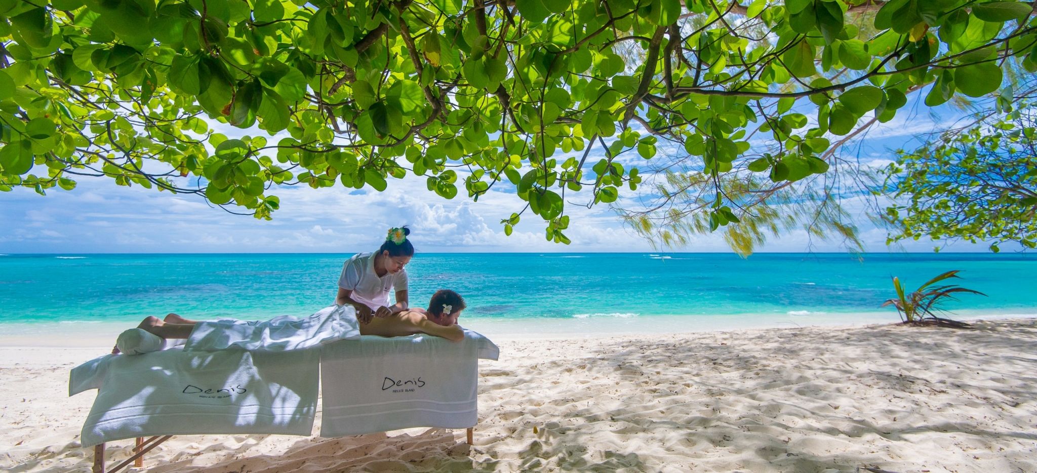 Eine Massage unter einem Takamaka-Baum am Strand auf Denis Island, Seychellen