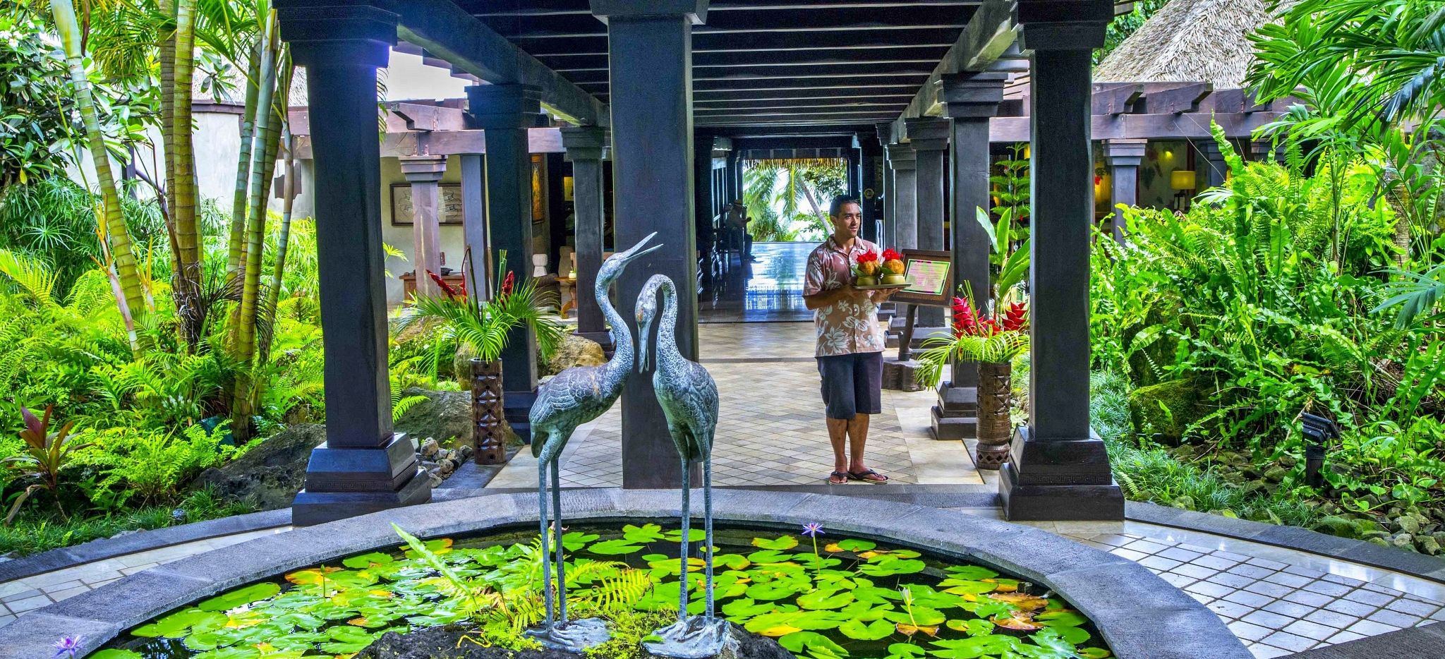 Eingang des Pacific Resort Aitutaki mit Kellner, welcher Willkommensgetränke in der Hand hält