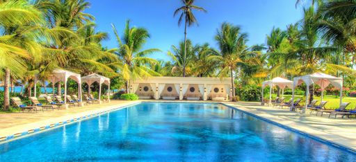 Ein Olympischer Pool, umringt von Sonnenschirmen, Strandliegen und einem omanisch-arabischem Haus