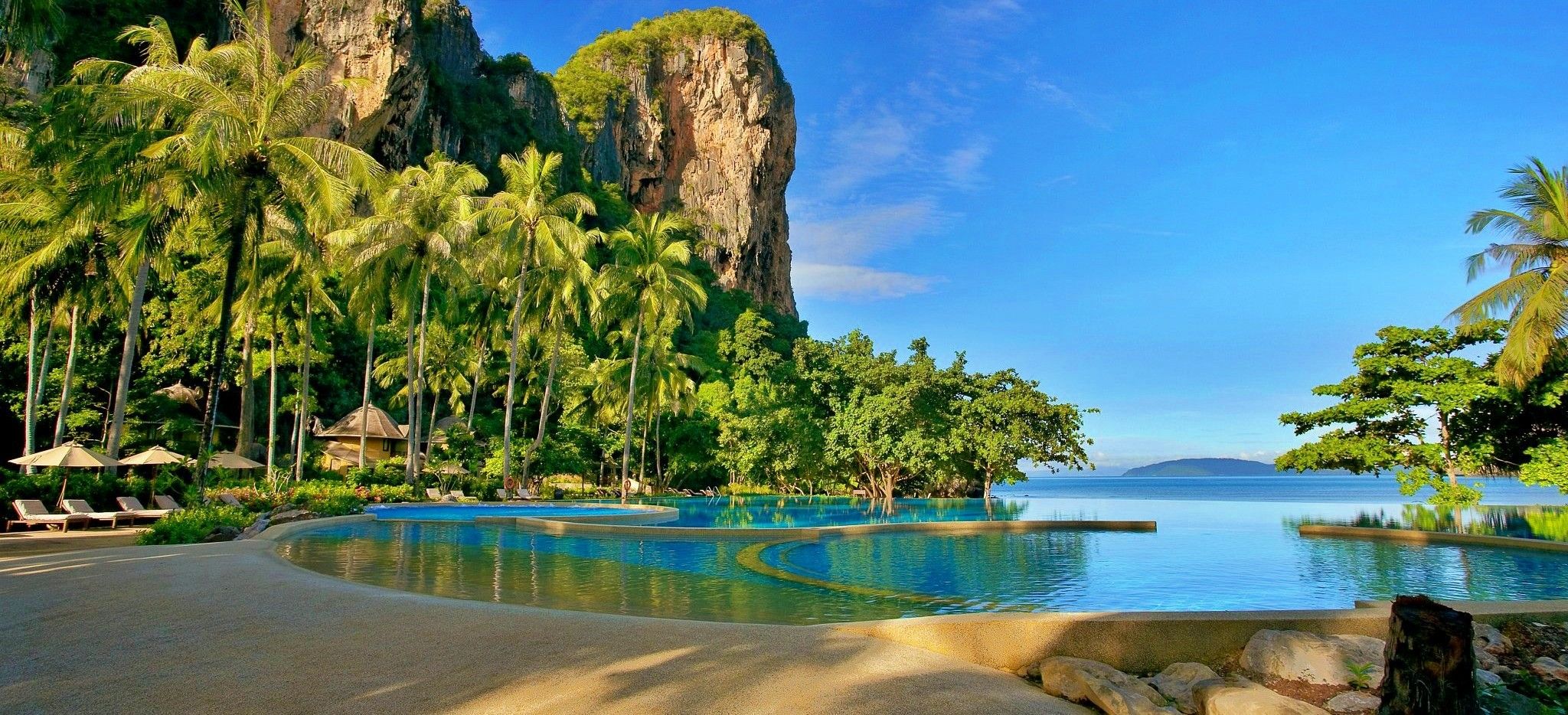 Ein Pool umgeben von Palmen und riesigen Felsen mit Blick auf das Meer