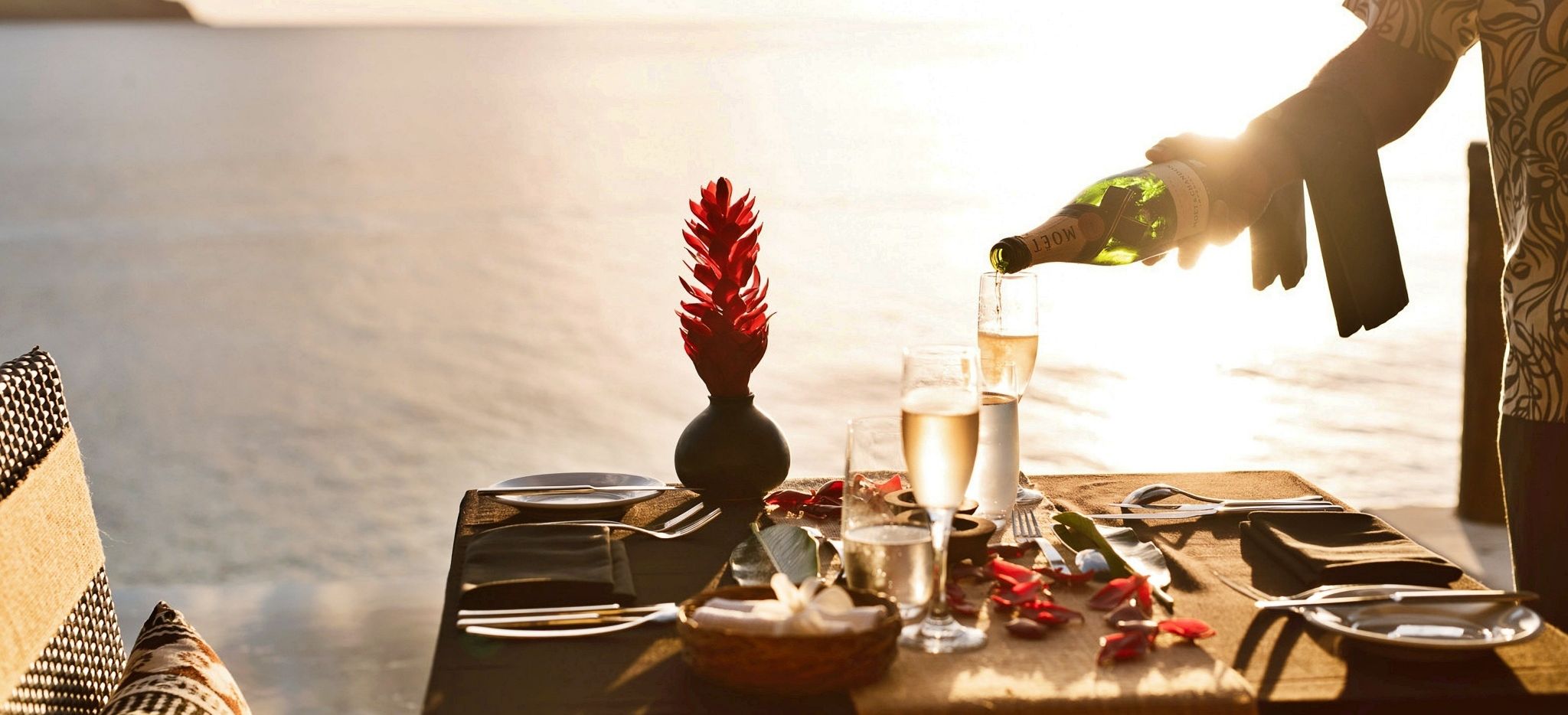 Ein Champagner auf dem Tisch wird vor der untergehenden Sonne eingeschenkt, Tokoriki, Fiji