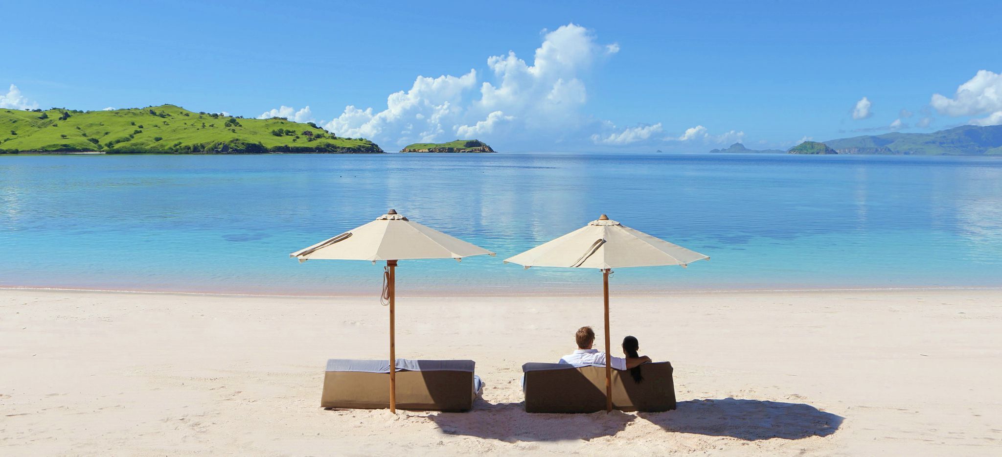 Paar auf Strandliegen am Strand, Blick auf das Meer und Inseln in der Ferne