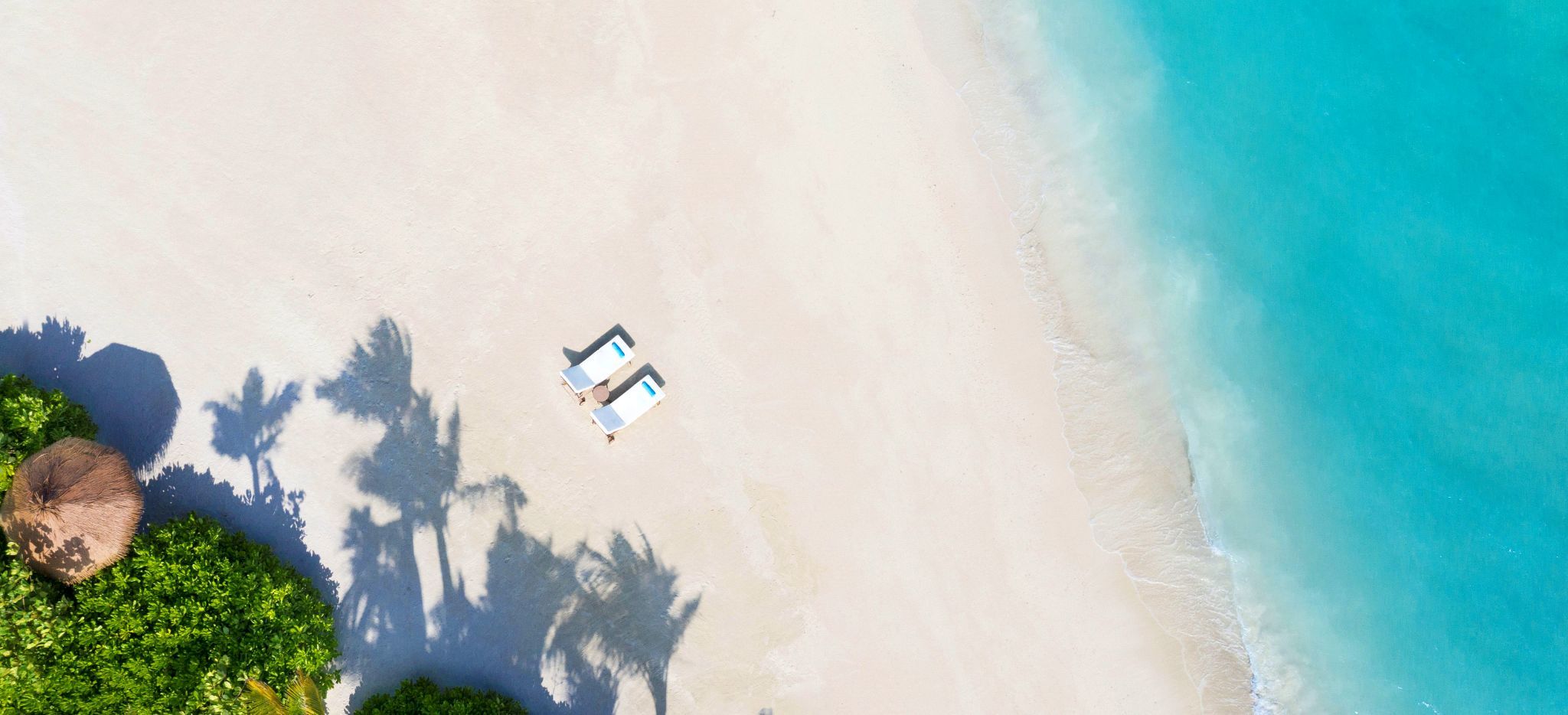 Ein Privater Strand mit zwei Strandliegen im Waldorf Astoria Maldives, mit ein wenig tropischem Grün