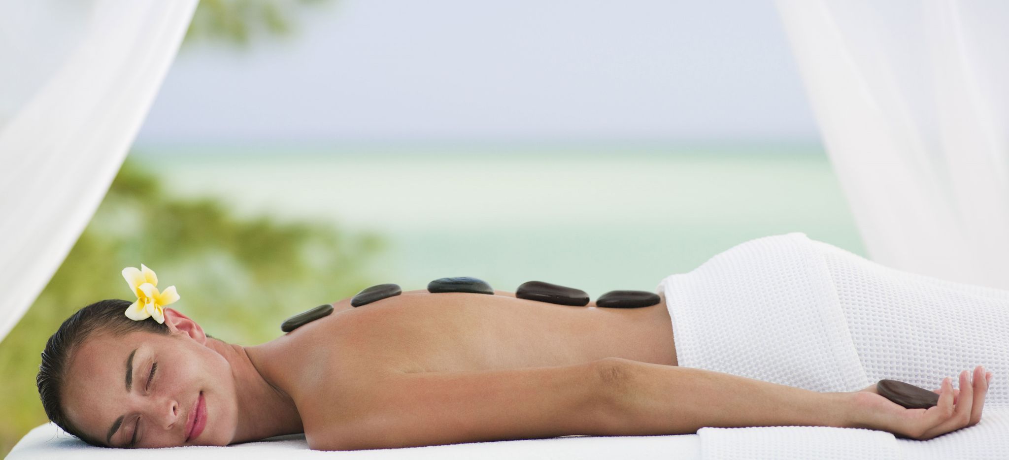 Eine Frau genießt eine Hot Stone Massage auf einer Liege am Strand