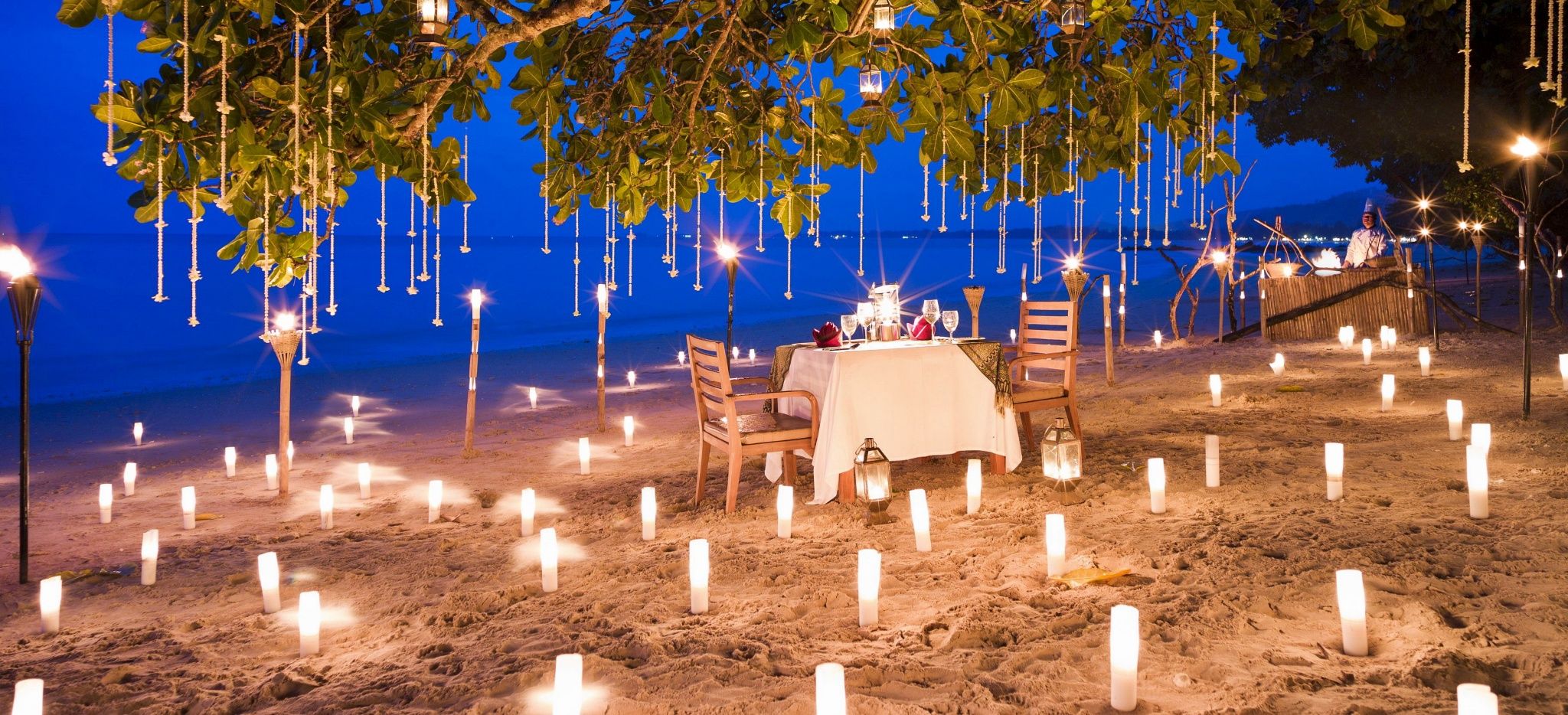 Ein Strand mit brennenden Kerzen, dazwischen ein Dinner Tisch. Im Hotel "The Sarojin"