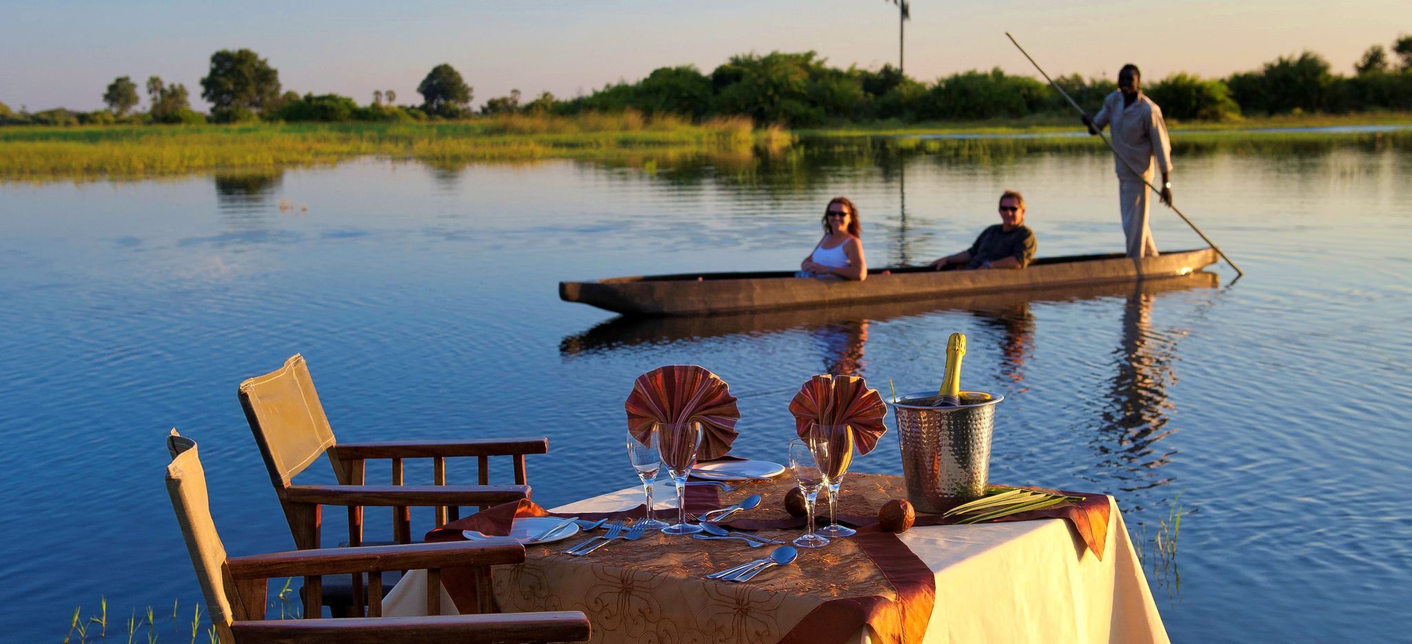 Paar mit Guide in Kanu, am Ufer ist ein Tisch für zwei gedeckt
