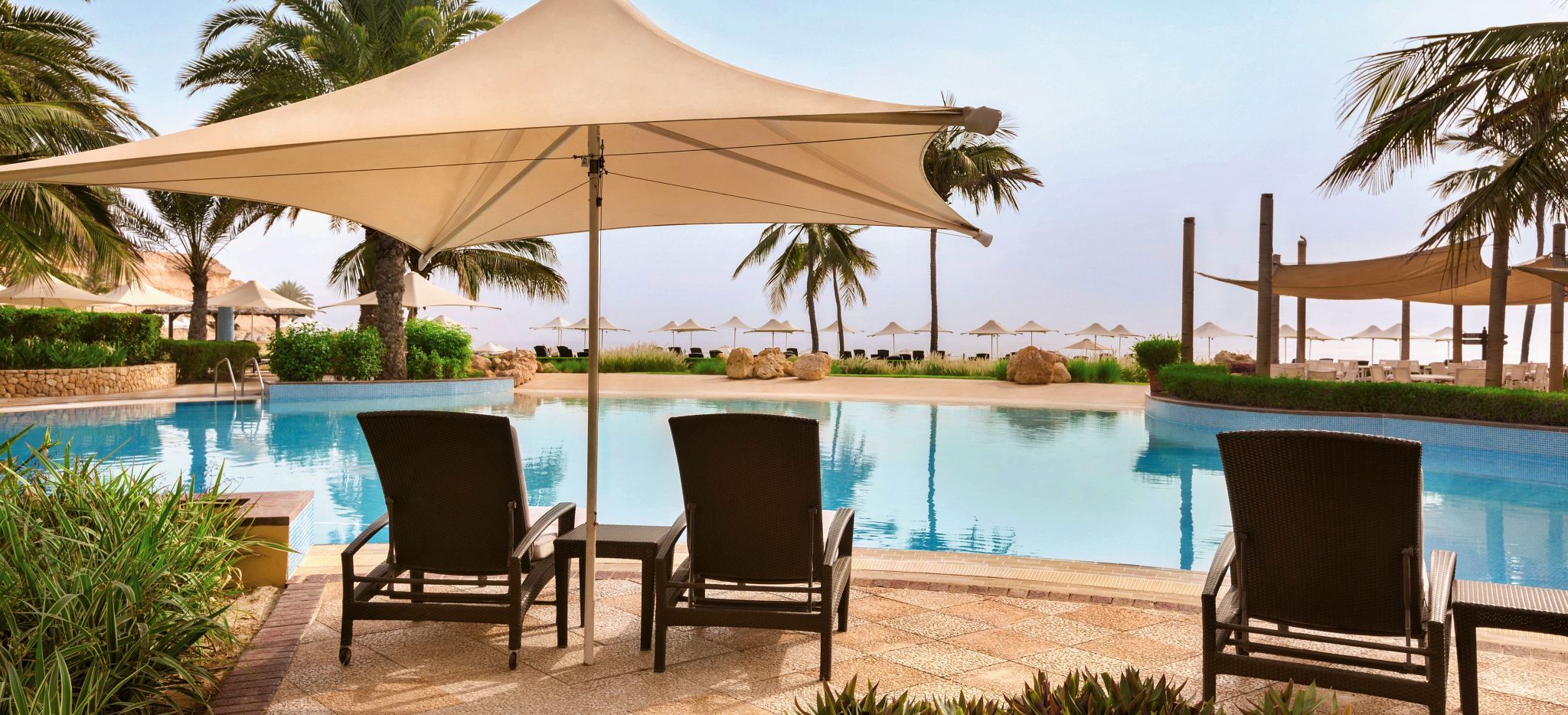 Pool mit Palmen und Sonnenschirmen und -stühlen im Shangri-La Barr Al Jissah Al Bandar Resort nahe Maskat, Oman