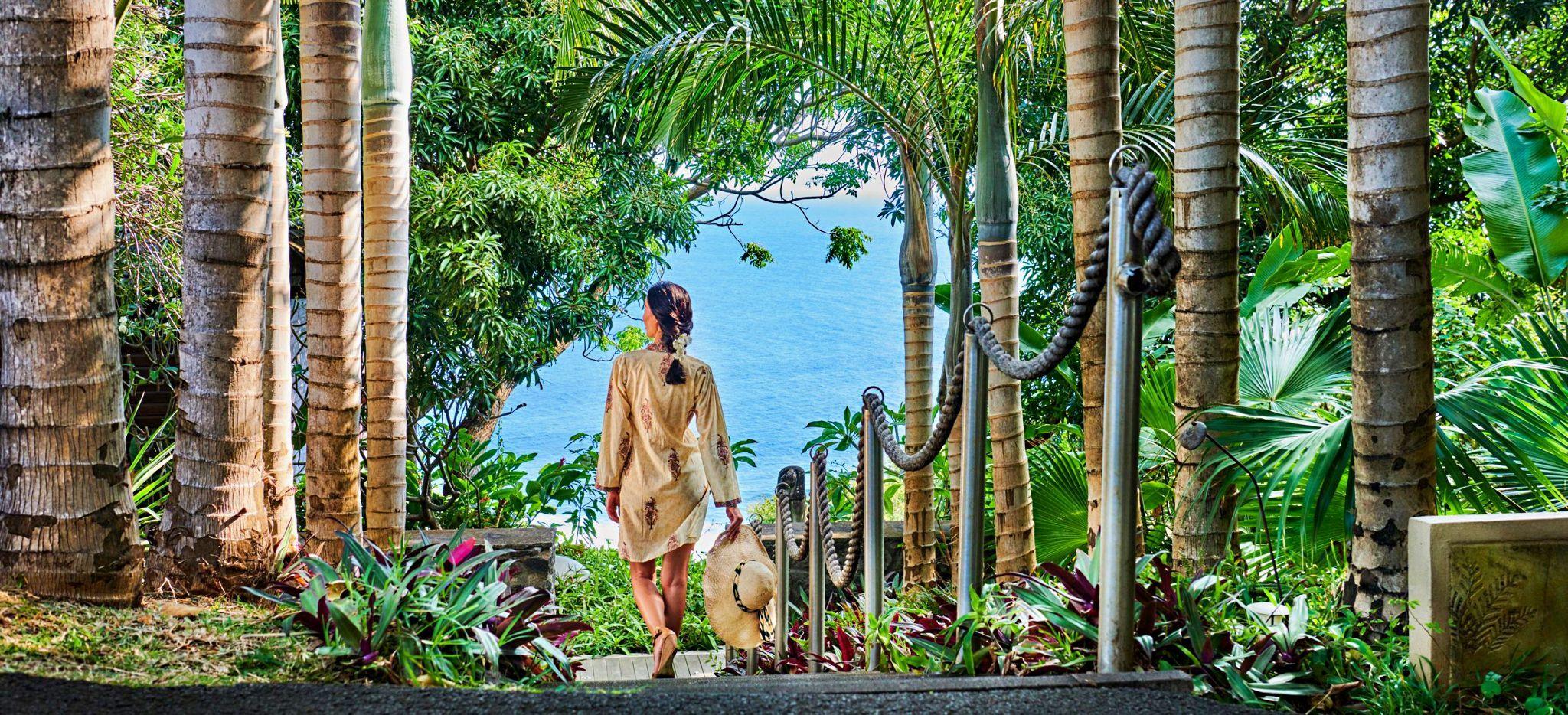 Eine Frau läuft die Treppen zwischen Palmen zu Meer im Hotel Palm auf La Réunion