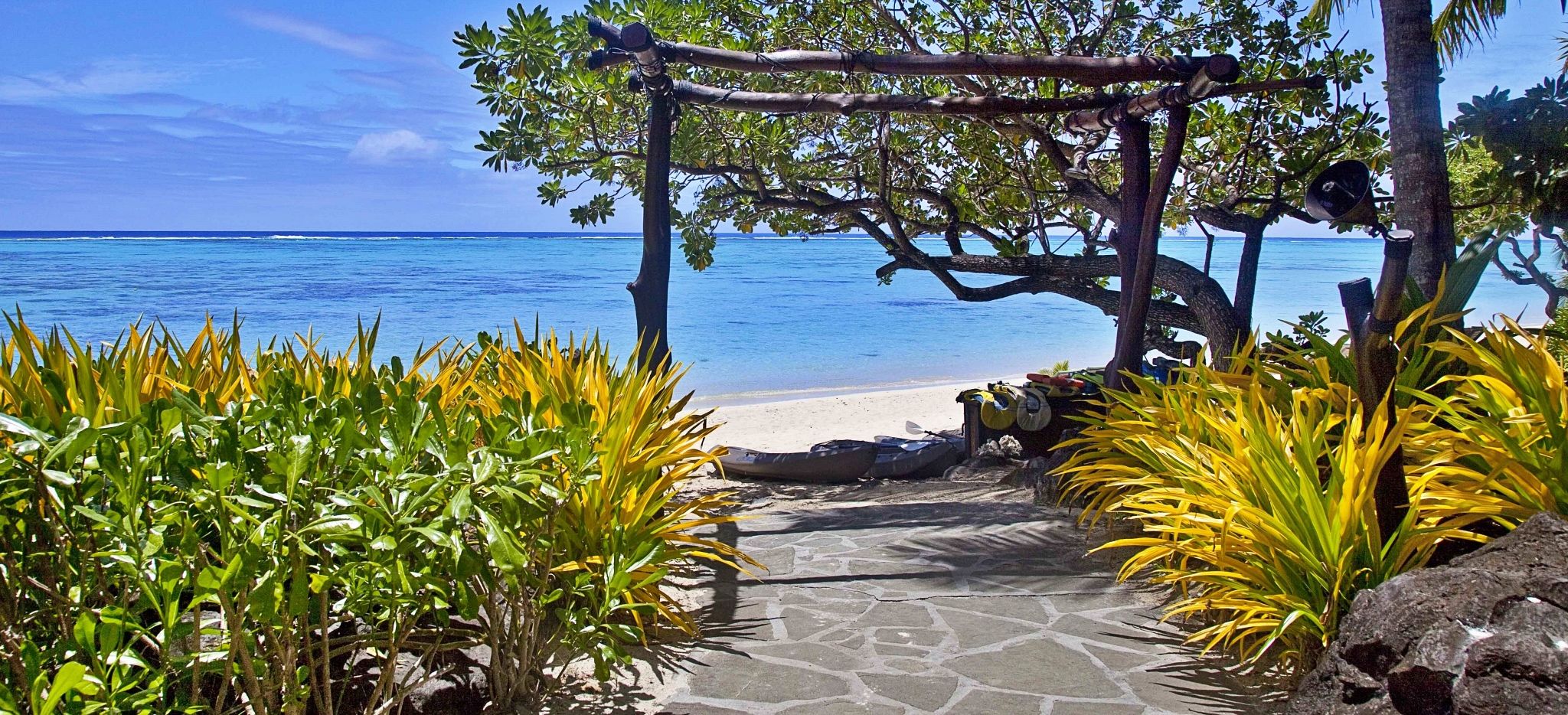 Torbogen am Strand des Pacific Resort Aitutaki mit Kanus und Meer im Hintergrund 