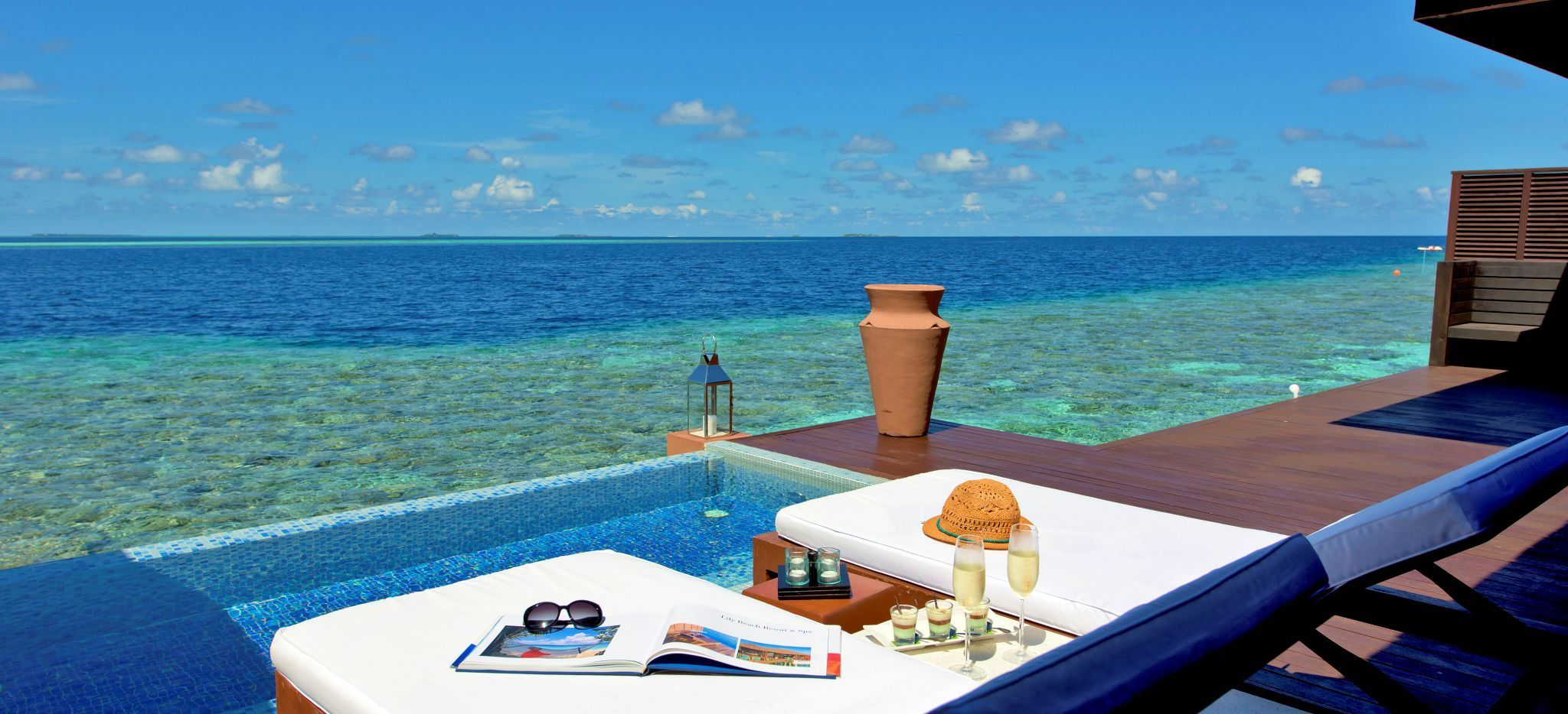 Zwei Strandliegen mit Magazinen und Champagner auf der Terrasse einer Wasservilla des Hotels "Lily Beach"