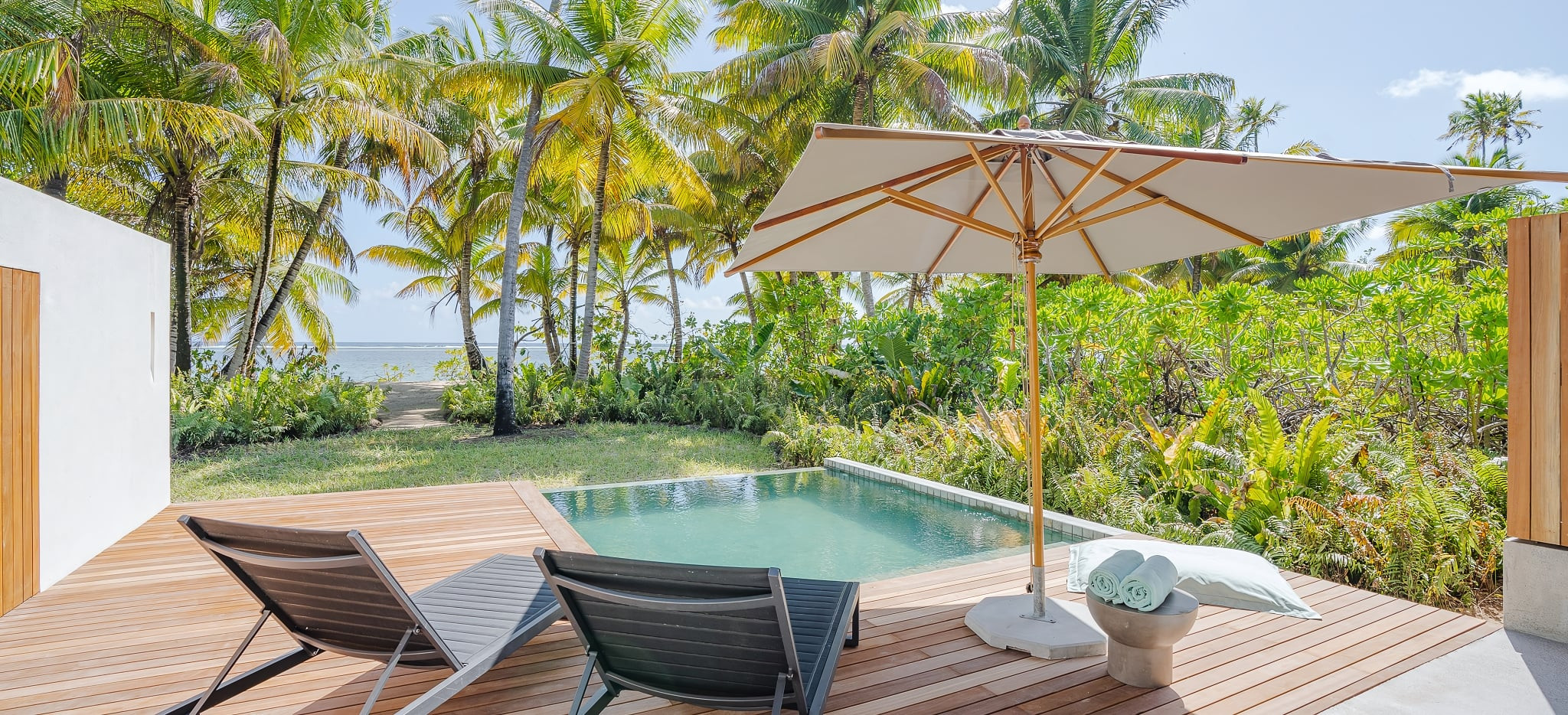 Der Blick über eine Terasse mit Sonnenstühlen und Sonnenschirm, einen privaten Pool, und dem Meerblick im Hintergrund. Ein Hotelzimmer der Kategorie Beach Villa im Hotel Alphonse Island Resort auf den Seychellen.