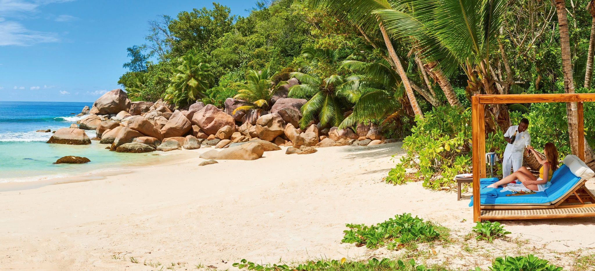 Eine Frau in einem Gazebo am Strand Petite Anse Kerlain bekommt von einem freundlichen Angestellten einen Drink gereicht