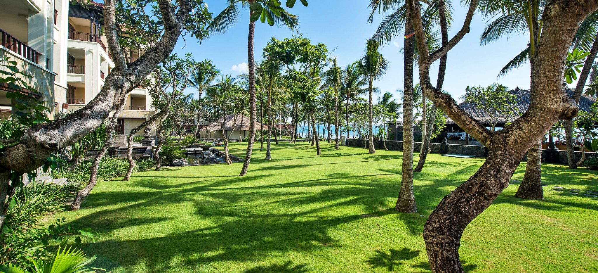 Ein grüner Englischer Rasen mit Bäumen im Hotel "The Legian"