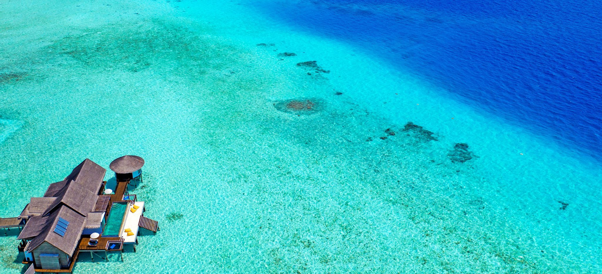 Eine große Wasservilla umgeben von flachem, türkisblauem Meer, vor der Insel Madhoo, Malediven