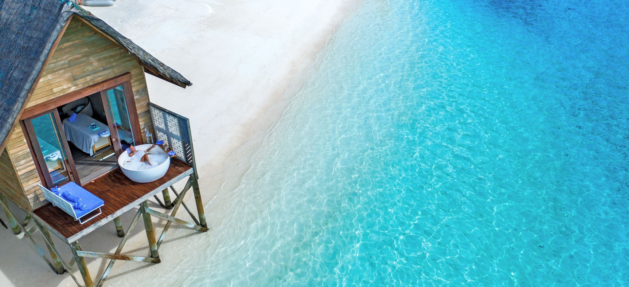 Eine Frau in einer Badewanne vor dem Wellnessbereich des Hotels OZEN auf den Malediven, mit Blick auf das Meer