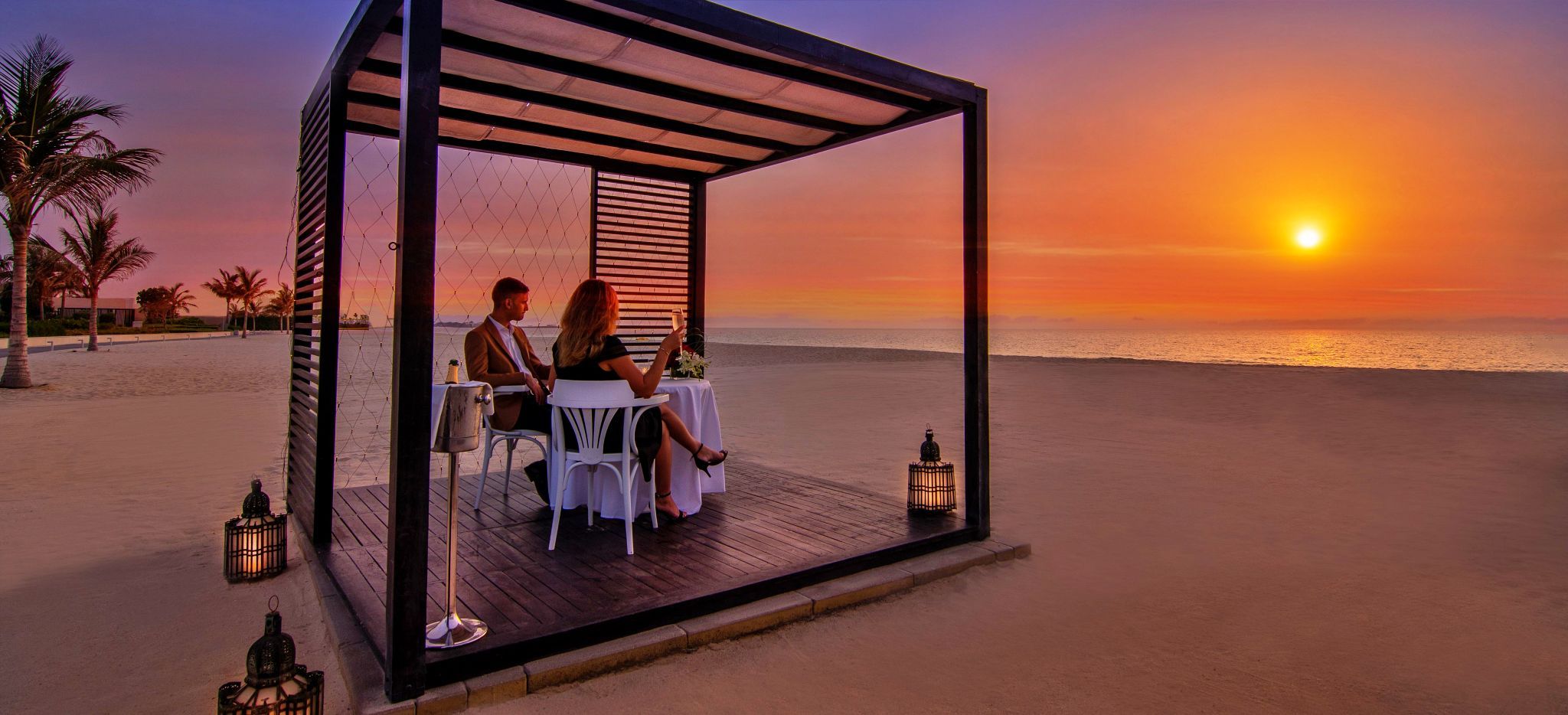 Ein Paar isst in einem Cabana am Strand zu Abend und beobachtet den Sonnenuntergang