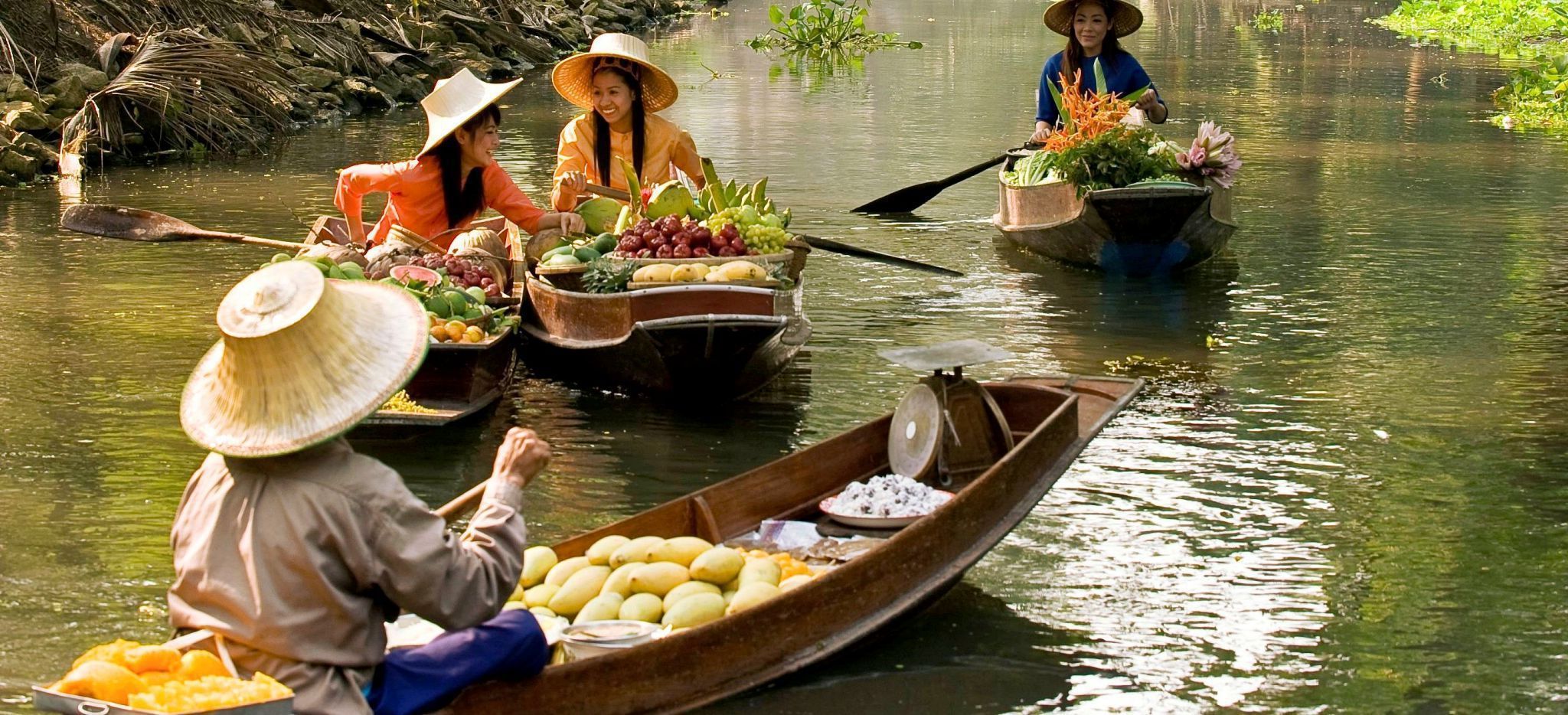 Frauen auf kleinen Ruderboten handeln mit Früchten und Gemüse in Thailand