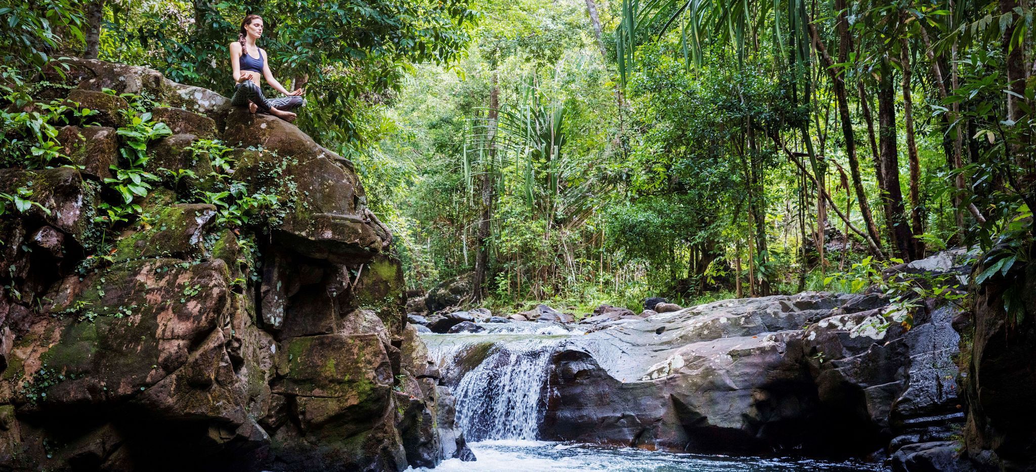 Eine Frau meditiert an einem Wasserfall am Crystal Creed nahe dem Hotel Datai Langkawi in Malaysia